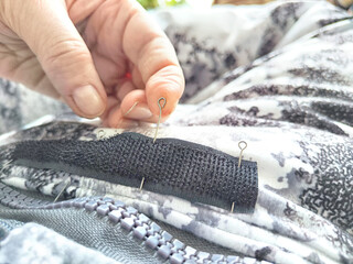 Sewing with a needle and thread on a mottled spotted fabric by hand. A middle-aged or mature hand...