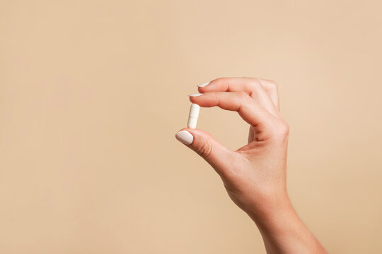 White pill in female hand on beige background, Taking Your Medication