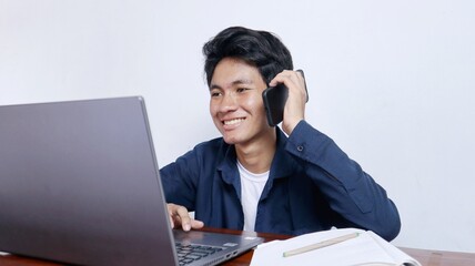 Young Asian male student is studying on a laptop, calling on the phone, doing assignments