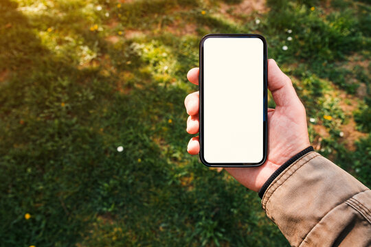 Smartphone mockup, male hand holding mobile phone with blank white screen in park on spring morning