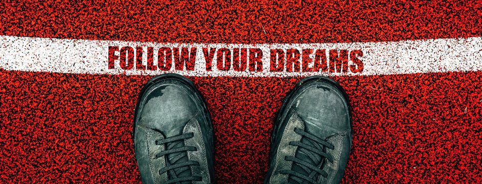 Follow your dreams text on rubber playground flooring, male boots from above standing next to the line