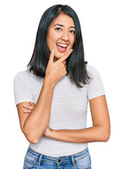 Beautiful asian young woman wearing casual white t shirt looking confident at the camera smiling with crossed arms and hand raised on chin. thinking positive.