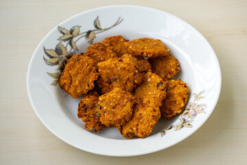 Crispy fried lentils with onion called Piyaju or Daler Bora on a white plate on a wooden background. Spicy onion fritters are made with lentil and onion which is a very popular snack in Bangladesh.