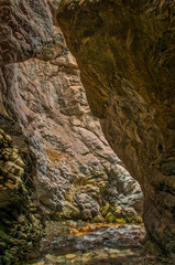 Fototapeta na wymiar Warm sunlight filters through a narrow canyon, illuminating a gentle stream below rocky walls