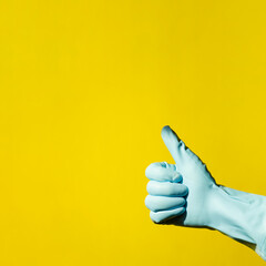 house cleaning concept. hand in blue rubber household glove shows gesture super - thumbs up on yellow background