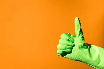house cleaning concept. hand in green rubber household glove shows gesture super - thumbs up on orange background