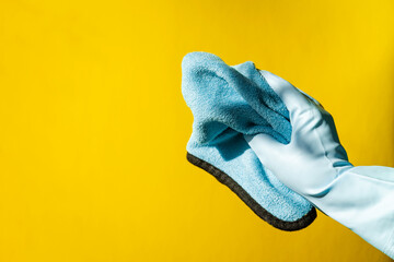house cleaning concept. hands in blue rubber household gloves hold rag on yellow background.