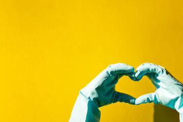 house cleaning concept. hand in blue rubber household glove shows gesture heart on yellow background.