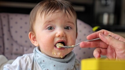 dirty baby eats porridge from a spoon. our dirty baby loves porridge and mess. happy family kindergarten kids concept. baby loves to eat porridge for breakfast. close-up baby eating porridge dream - 767821717