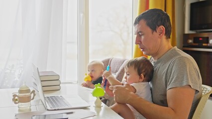 father working from home remotely with baby daughter in his arms. pandemic remote work business a concept. father tries to work at home in fun kitchen, baby children interfere sitting on their hands - 767821907