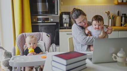 mother working from home remotely with baby daughter in his arms. pandemic remote work business a concept. mother tries to work at home in kitchen, baby children interfere sitting on their fun hands - 767822321