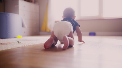 baby learns to crawl on the floor at home. happy family kindergarten kids concept. First steps, baby crawling view from the back. baby learns to crawl to explore the world around dream him - 767823768