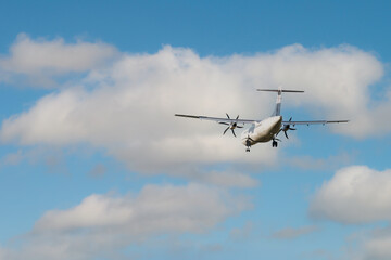 Rear view of an ATR 72 airplane among the clouds.  Twin-engine turboprop short-haul regional passenger aircraft. Landing airplane.