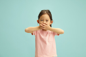 Child Covering Mouth with Hands Stands Against Blue Isolated 