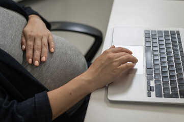 A pregnant woman works on a laptop in the office. Close-up of the tummy. 