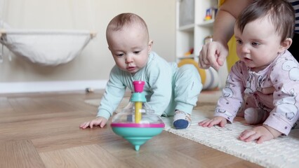 baby group playing spinning top toy. kindergarten a happy childhood concept. baby twins with mom play toy whirligig indoors. baby group in kindergarten with a teacher play top in lifestyle playroom - 767826125