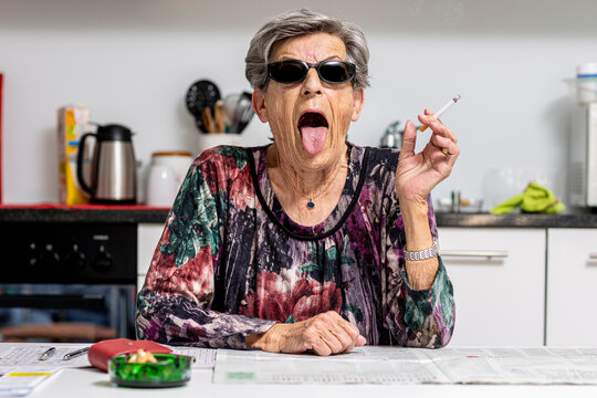 Woman sitting at the table with a cigarette in her hand while grimacing