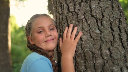 a small child ecologist hugs the trunk of a tree bark in a forest park. the gentle touch of a child on the trunk of the tree of life. Nature in caring hands lifestyle: children protect the forest - 767828986