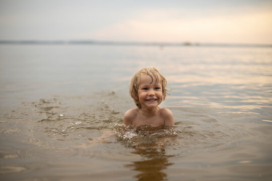 A three-year-old fair-haired boy bathes outdoors on a summer evening in the water, Holidays with children, restoration and relaxation in nature, development of children's scientific and cognitive acti