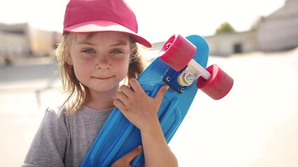 child with a skateboard. girl in a red cap with a skateboard on the playground portrait. skateboarder child close-up outdoors sun glare. kid skateboarder looking at the camera lifestyle - 767830558