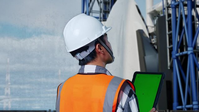 Close Up Back View Of Asian Male Engineer With Safety Helmet Working On A Green Screen Tablet And Looking Around While Standing With Space Shuttle