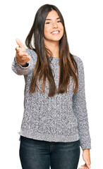 Young brunette woman wearing casual winter sweater smiling friendly offering handshake as greeting and welcoming. successful business.