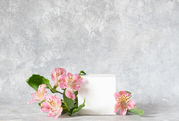 Cosmetic background. Cubic white podium and flowers alstroemeria on a gray backdrop. Mockup for the demonstration of natural body care products. copy space