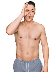 Fototapeta premium Handsome young man wearing swimwear shirtless doing ok gesture shocked with surprised face, eye looking through fingers. unbelieving expression.