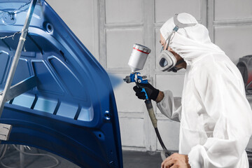 Male Industrial worker sprays paint using airbrush gun on part of car wears in protective mask and...