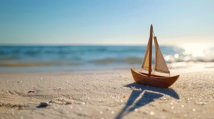 Rolgordijnen Miniature sailboat model on a sandy beach with a blurred ocean background. © Moopingz