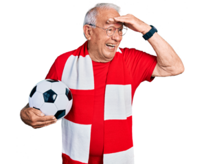 Senior man with grey hair football hooligan holding ball very happy and smiling looking far away with hand over head. searching concept.
