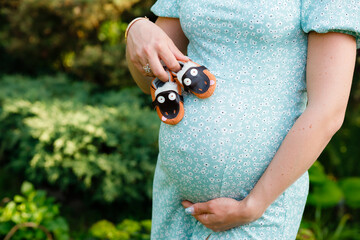 A pregnant woman hugs her tummy and holds baby shoes