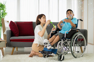 Portrait of enjoy happy love family asian mother playing and carer helping look at disabled son child sitting in wheelchair moments good time at home.disability care concept