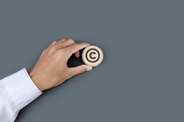 A businessman's hand holds a wooden badge with a copyright symbol engraved. Property rights and brand patent protection in business concept.