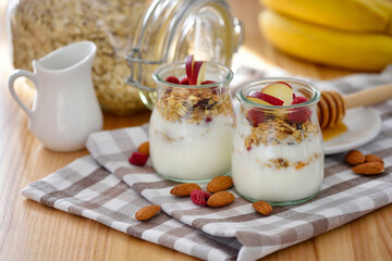 Crunchy granola with yogurt, apple, nuts and banana in glass jars on wooden table. Healthy breakfast concept. - 767840152