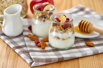 Crunchy granola with yogurt, apple, nuts and honey in glass jars on wooden table. Healthy breakfast concept. - 767840177
