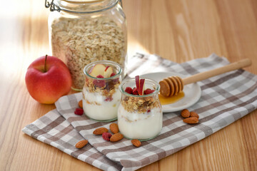 Crunchy granola with yogurt, apple, nuts and honey in glass jars on wooden table. Healthy breakfast concept. - 767840192