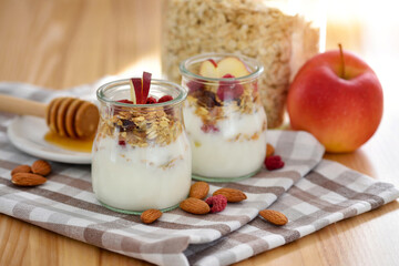 Crunchy granola with yogurt, apple, nuts and honey in glass jars on wooden table. Healthy breakfast concept. - 767840193