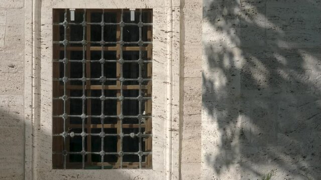 Glass window with metal bars on the facade of an old stone building on a sunny day
