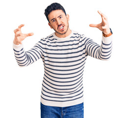 Fototapeta premium Young hispanic man wearing casual clothes shouting frustrated with rage, hands trying to strangle, yelling mad