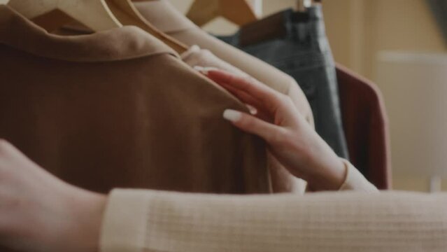 Cropped slowmo shot of unrecognizable stylish woman choosing her ootd while looking through fashionable clothes hanging on rail