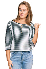 Beautiful blonde woman wearing casual clothes smiling with happy face looking and pointing to the side with thumb up.