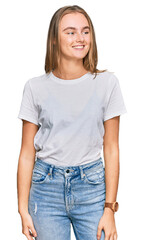 Obraz premium Beautiful young blonde woman wearing casual white t shirt looking away to side with smile on face, natural expression. laughing confident.
