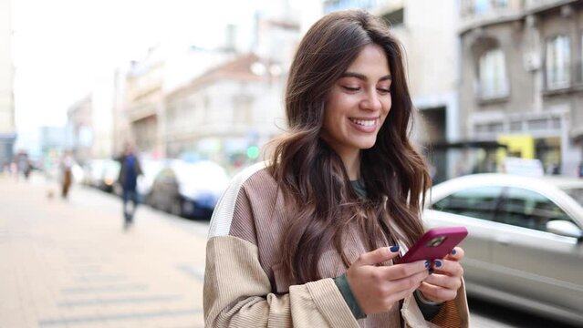 Happy Spanish girl walking and using smartphone