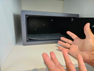 Empty open safe in a hotel room or home and the hands of a guest