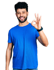 Young arab man with beard wearing casual blue t shirt smiling positive doing ok sign with hand and fingers. successful expression.