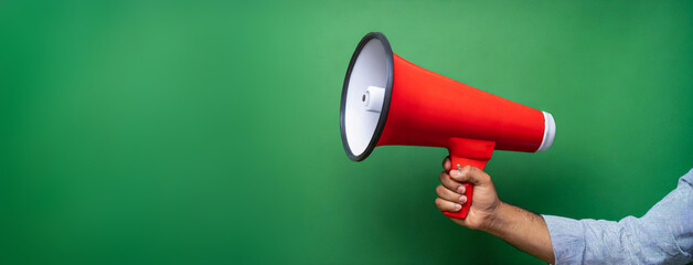 Hand holds a red megaphone isolated on green background. Concept of communication, message, announce
