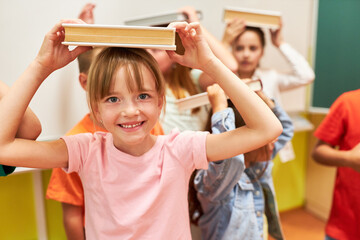 Smiling girl balancing book on head in class