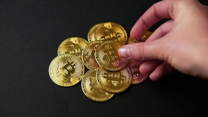 Hand leaving a bitcoin on a pile of bitcoins golden coins on a black background. Bullish BTC, cryptocurrency, 2p2 exchange and blockchain concept