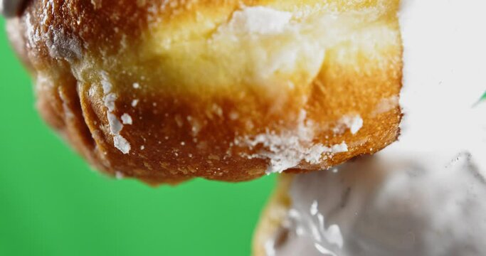 Donut with dripping white icing. Stock clip. Close-up baking with stream of white cream. White cream drips from bun on green background. Baking and cooking